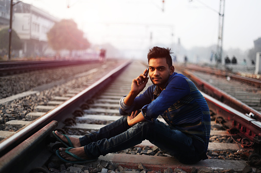 Young man sitting in the middle of railroad track and talking on mobile phone.