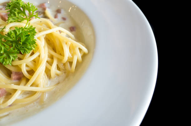 istock Spaghetti white creamy sauce with ham and mushroom on white dish with black background