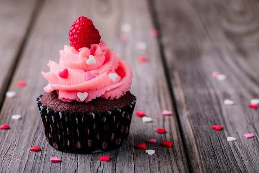 Chocolate cupcakes with pink cream, sugar hearts and fresh raspberries for St. Valentine's Day