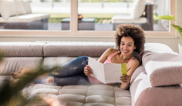 istock Relaxed black woman reading a magazine on sofa at home. 902820588