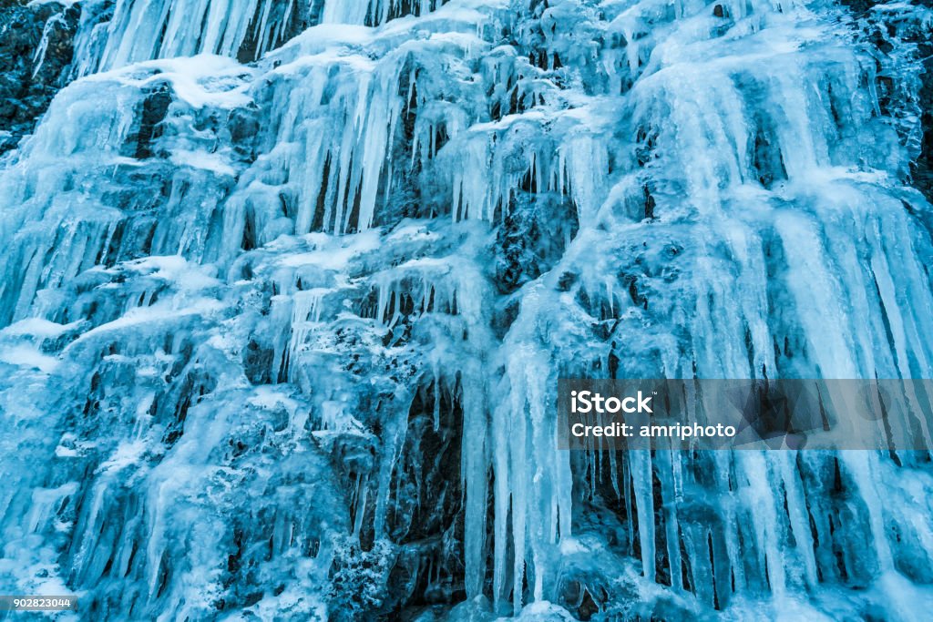 4 Seasons - many huge icicles over rock face on cold winter day wall of many big icicles representing cold weather winter eery spooky atmosphere ice palace low perspective Arctic Stock Photo