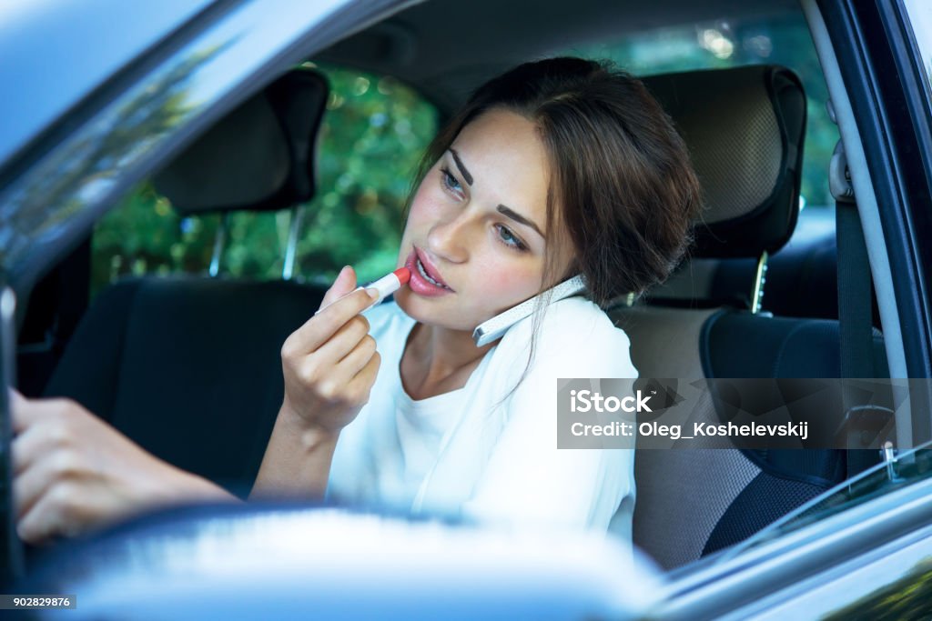 busy girl with lipstick and phone while driving busy pretty girl with lipstick and phone while driving Driving Stock Photo