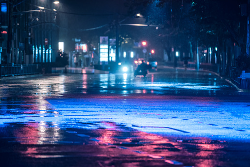 Cars driving on wet road in the rain and colored lights reflected on the wet asphalt road