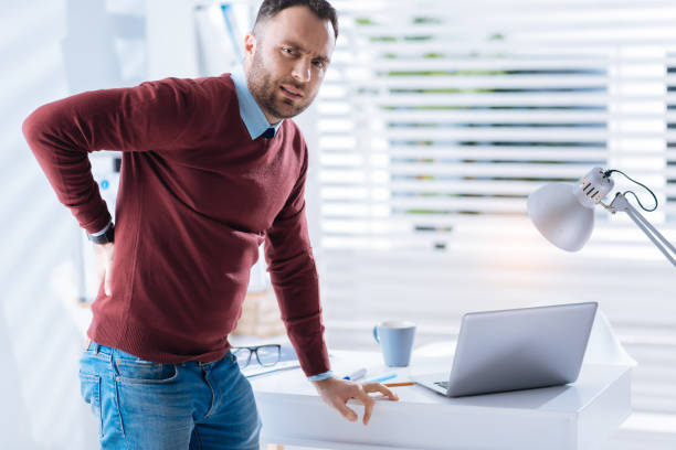 istock Upset man standing next to the table and touching his aching back 902830478