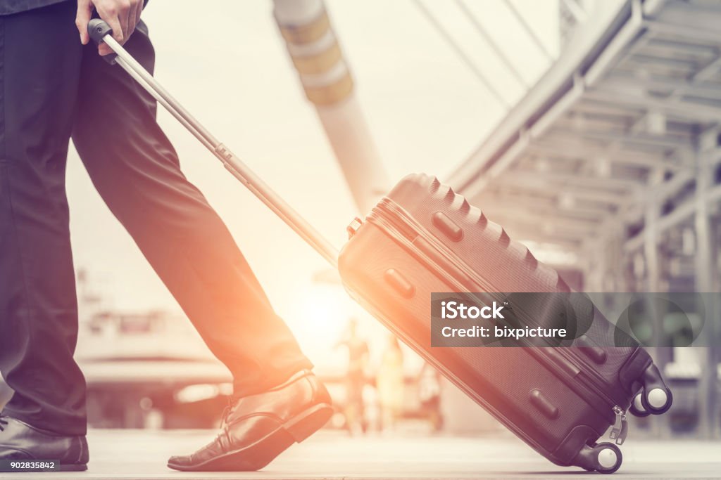 Businessman drag luggage and hold suit in city outdoor on building background. Concept of business trip and work life balance. Image processing vintage color. Travel Stock Photo