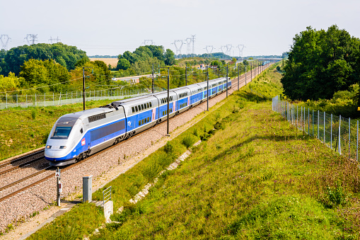 Moisenay, France - August 23, 2017: A double-decker TGV Duplex high speed train in Atlantic livery from french company SNCF driving on the Southeast TGV line along the A5 highway in the countryside.