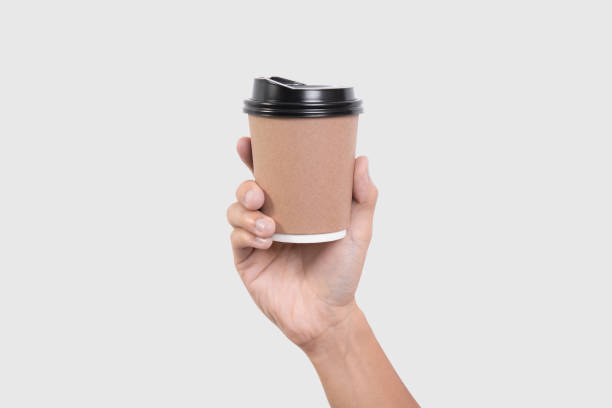 istock hand holding coffee paper cup isolated on grey background. mock up for branding. 902842844