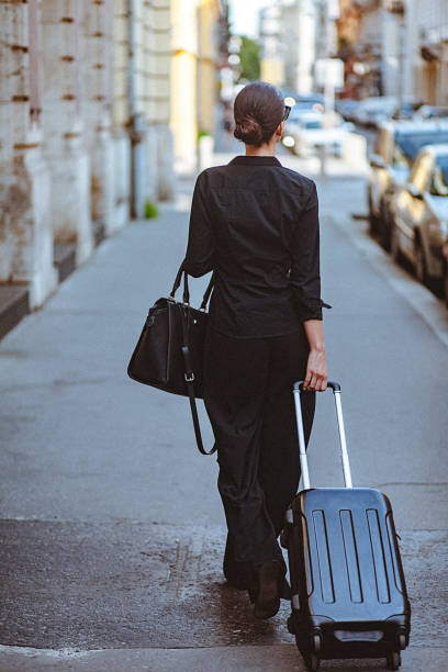 istock Rear view of a young woman walking down the street and pulling a small suitcase 902847100