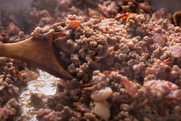 Bacon picado e chão carne fritar em uma frigideira com uma colher de pau - foto de acervo