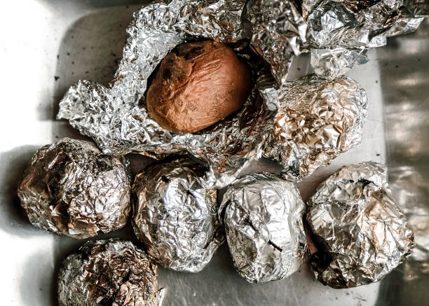 Potatoes wrapped with aluminium foil cooked with the ember of a barbecue servetd on metal plate.