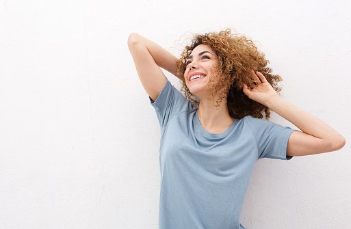 Portrait of happy woman laughing with hand in hair against white wall