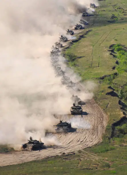 Many T-80 tanks move down the hill in a cloud of dust in summer