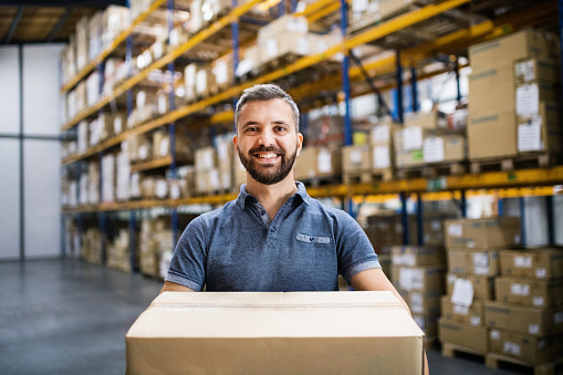 Young male warehouse worker or a supervisor holding a large box.