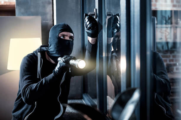 masked burglar breaking into the house - burglary imagens e fotografias de stock