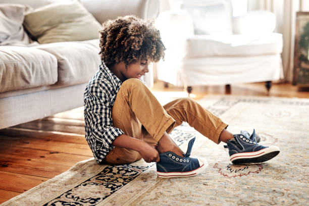 I have to get ready for school Shot of a determined young little boy trying to put on his shoes inside at home during the day child tied up stock pictures, royalty-free photos & images