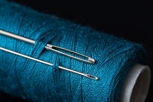 coil of dark blue thread and two needles macro