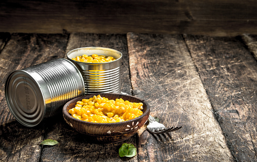Canned corn in a tin can with fork. On a wooden background.