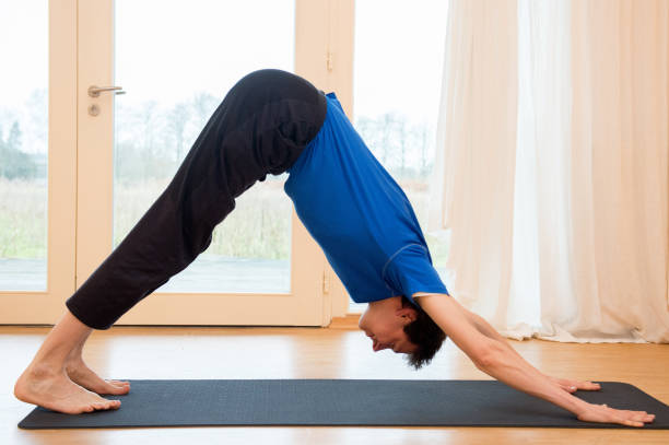Man practicing yoga indoors Man practicing yoga indoors in a retreat space doing Downward-Facing Dog Pose - Adho Mukha Svanasana downward facing dog position stock pictures, royalty-free photos & images