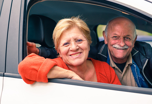 Senior couple enjoying their new car - Happy people smiling during road trip vacation - Active elderly concept around the world - Focus on woman - Warm filtered look