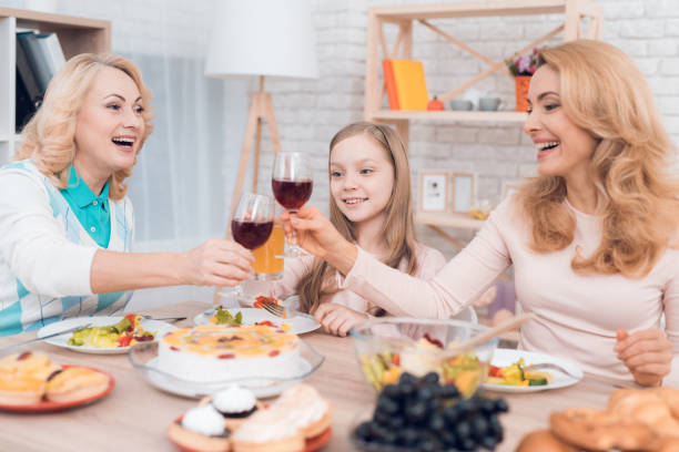 mom and grandmother are drinking wine, a little girl is drinking juice. - drinking little girls women wine imagens e fotografias de stock
