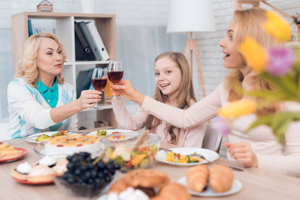 mom and grandmother are drinking wine, a little girl is drinking juice. - drinking little girls women wine imagens e fotografias de stock