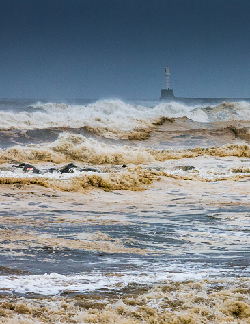 Huge waves crash against the lighthouse breakwater.  The location is the North Sea, Aberdeen, Scotland.  It is Winter and extreme weather storms often batter the city defences.  The sea is raging and the sky is dark.