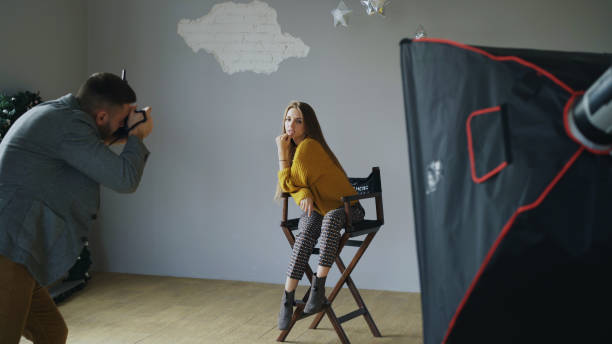 istock Young beautiful woman model posing for photographer while he is shooting with a digital camera in photo studio indoors 902920854