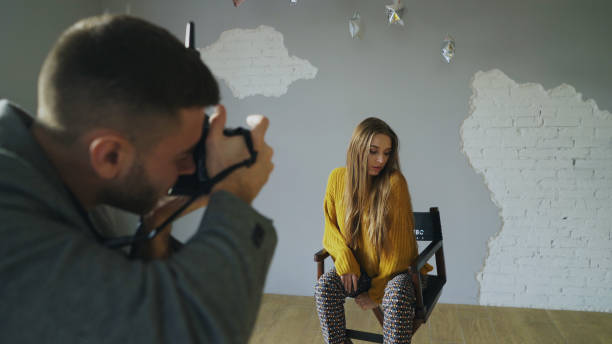 istock Young beautiful woman model posing for photographer while he is shooting with a digital camera in photo studio indoors 902920998