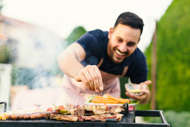 Grilling Smiling man seasoning meat on the grill salt seasoning stock pictures, royalty-free photos & images