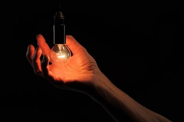 istock Incandescent light bulb in a hand on a black background. 902928952