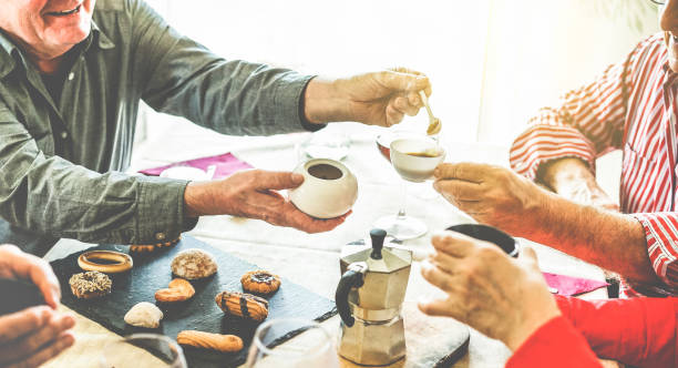 Group of senior people toasting italian style moka coffee after lunch - Mature happy friends eating biscuits and laughing together - Focus on men bottom hands - Warm contrast cine filter Group of senior people toasting italian style moka coffee after lunch - Mature happy friends eating biscuits and laughing together - Focus on men bottom hands - Warm contrast cine filter moka stock pictures, royalty-free photos & images