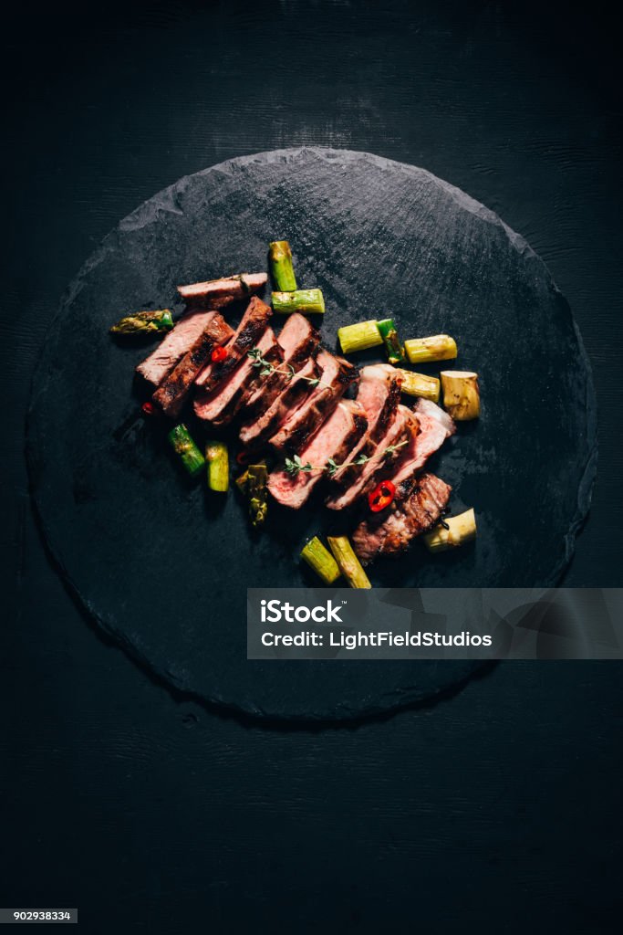 vue de dessus de savoureuses tranches viande grillée aux asperges sur ardoise noire - Photo de Haute gastronomie libre de droits