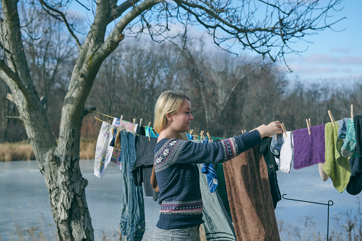 Blond woman hanging laundry to dry outdoors on a line hanging from a tree to the house. Retro style clothes