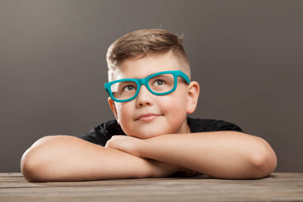 istock Smiling teenager boy with eyeglasses leaning on table 902954062