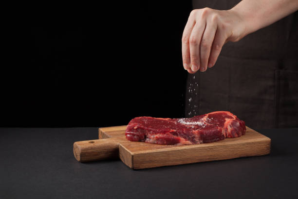 istock Beef steak and salt by chef on the background with free space for text design or logotype menu restaurant. Food background. Black text area. Copy space 902957598
