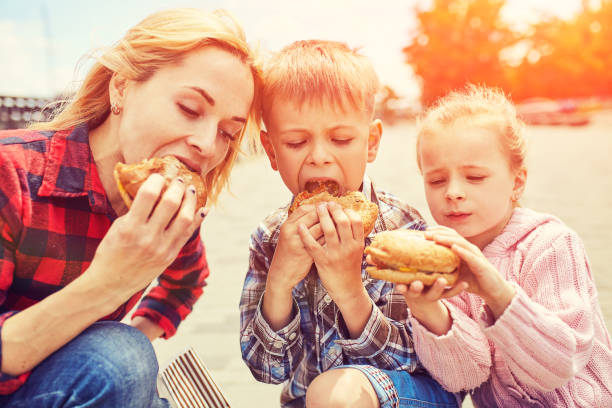 Mom and children eating a hamburger outdoors stock photo