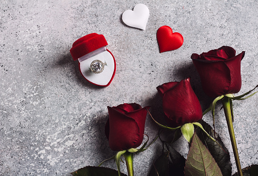 Valentines day marry me wedding engagement ring in box with red rose gift surprise on grey background with copyspace. Love flower gift for woman making proposal on romantic holiday wedding