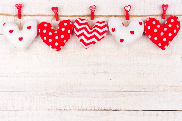 istock Valentines Day handmade cloth heart pillows on a line over white wood 902994010