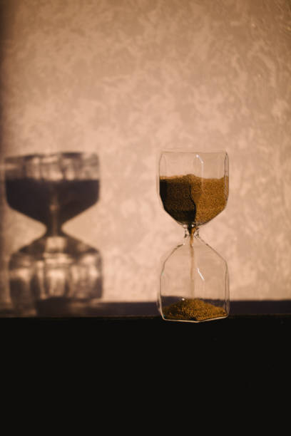 istock Hourglass with shadow on wall. Time passing concept for business deadline, urgency and running out of time. Sandglass, egg timer showing the last minute or time out. Copy space for text and design 902995232