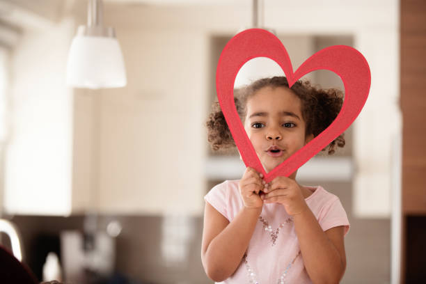portrait of a little girl in a red beret and clothes on a background of colorful hearts holding a heart, a smiling child, the concept of Valentine's day