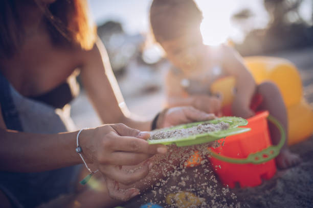 Young mother and baby daughter sieving sand at the beach
