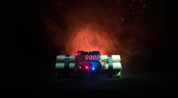 istock Image of a time bomb against dark background. Timer counting down to detonation illuminated in a shaft light shining through the darkness 903040276