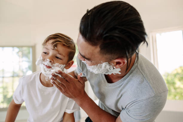 istock Man applying shaving foam in his sons face 903049482