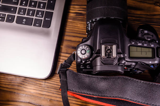 istock Modern DSLR camera and laptop on wooden table. Top view 903050288