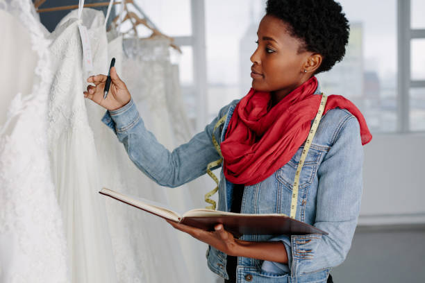 Female bridal store owner looking at wedding gown Female bridal store owner looking at wedding gown with a diary in hand. Dressmaker with diary examining bridal wear pattern. bridal shop photos stock pictures, royalty-free photos & images