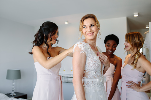 Bride and bridesmaids during the wedding preparations. Friends dressing the bride for wedding in a hotel room.