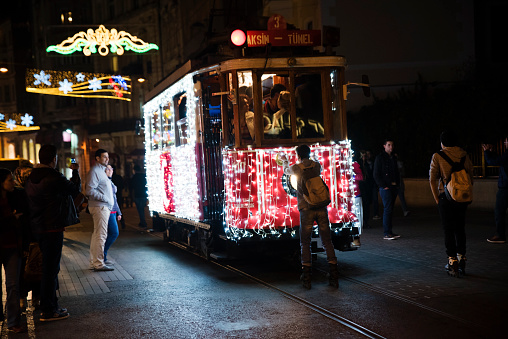 Istanbul, Turkey - November 06, 2014: A Nostalgic Taksim Tram was adorned with Christmas lights at The Famous Istiklal Street, Pera, Istanbul. A skater boy was holding the tram's headlight. Also people were watching the scene.
