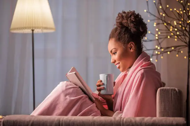 Photo of Cheerful african girl enjoying literature and hot beverage