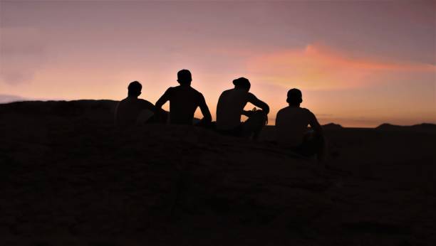 istock Silhouette Male Friends Sitting On Field During Sunset 903110990