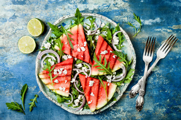 verão fresco grelhado salada de melancia com queijo feta, rúcula, cebolas em fundo azul - queijo feta - fotografias e filmes do acervo